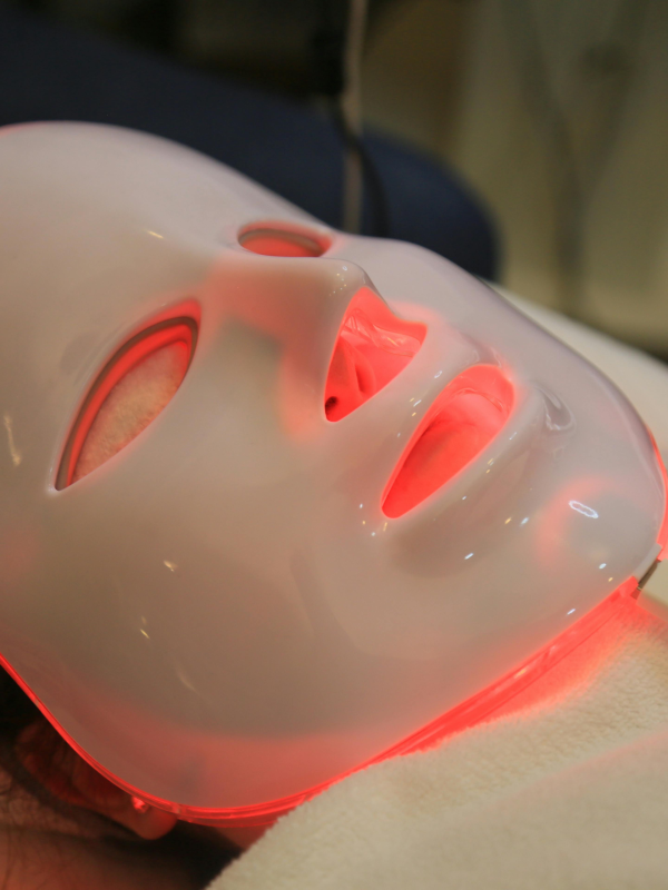 Woman wearing a white LED red light therapy face mask glowing red during an at-home anti-aging skincare treatment