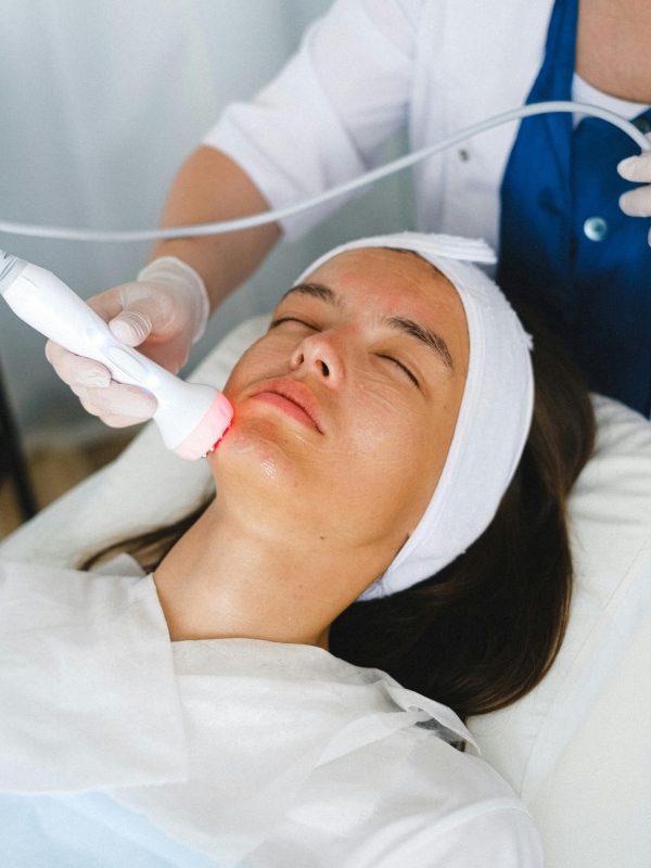 Esthetician applying a red light therapy wand to a woman's face during a professional skin rejuvenation treatment
