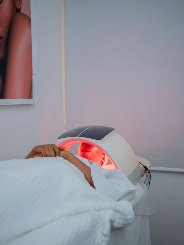 Woman lying down using an LED red light therapy face mask device during a home skincare treatment session